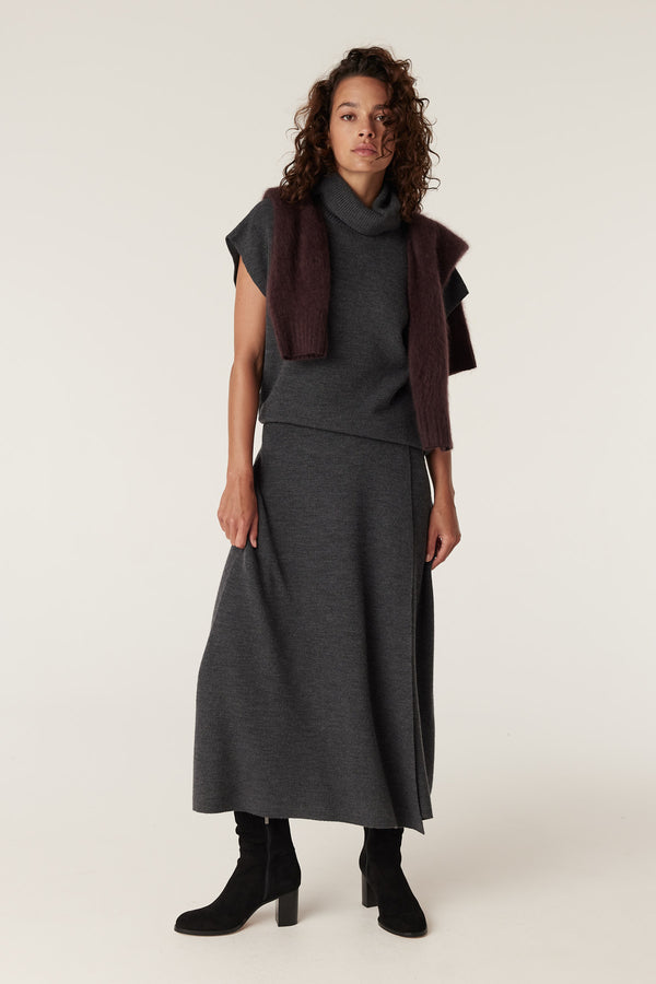 Woman wearing a charcoal merino midi skirt and matching turtleneck top, with a brown sweater draped over her shoulders.