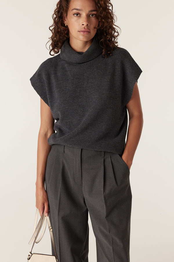 Woman in a charcoal merino wool sleeveless turtleneck top and dark grey pleated trousers.