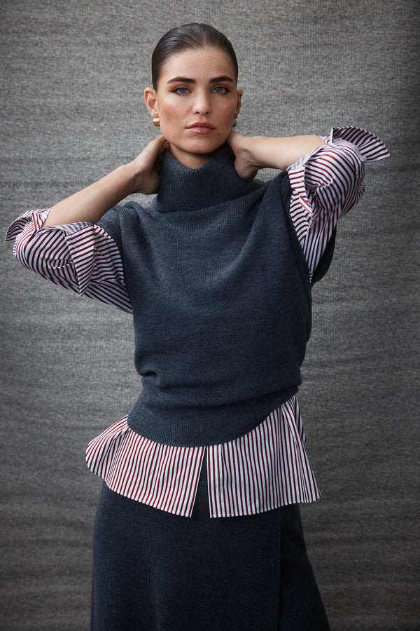 Woman in charcoal Eloise Merino turtleneck top layered over a red and white striped shirt.
