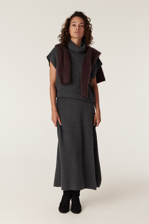 Woman in charcoal merino wool turtleneck top, matching maxi skirt, and a brown sweater draped over shoulders.