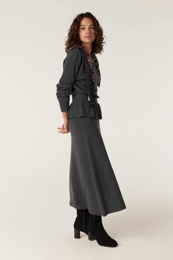 Woman in charcoal merino peplum jumper and matching skirt, black boots, and patterned scarf.