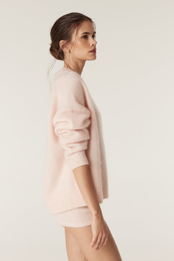 Woman in a soft pink mohair blend V-neck jumper with ribbed cuffs and hem, paired with matching shorts.