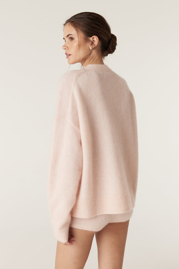 Woman wearing a soft pink mohair blend V-neck jumper with ribbed cuffs and hem, paired with matching shorts.