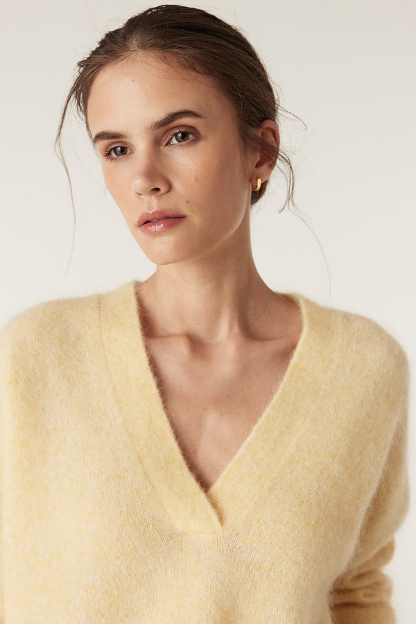 Woman wearing a soft, butter yellow mohair blend V-neck jumper with a relaxed fit.