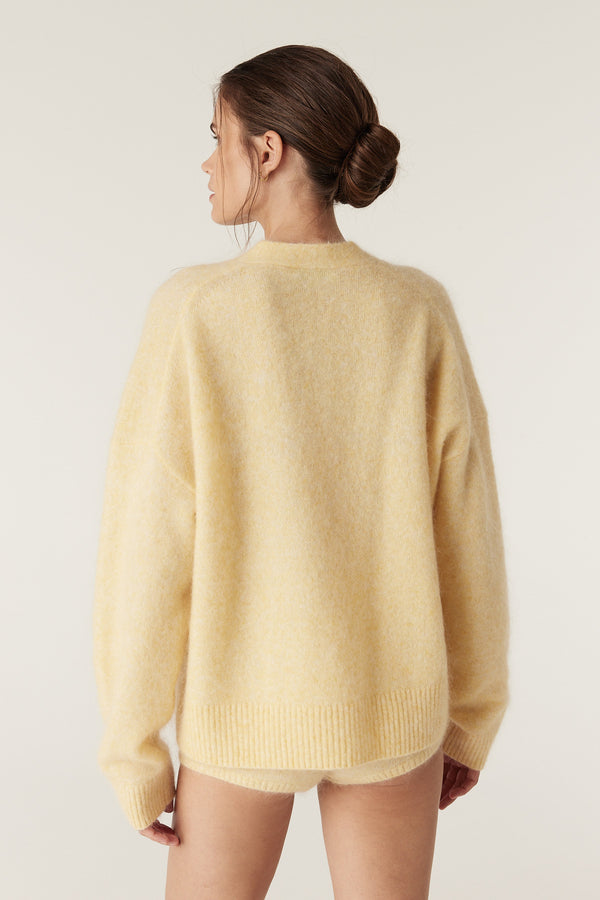 Model from behind wearing a butter yellow mohair blend V-neck jumper with ribbed cuffs and hem.