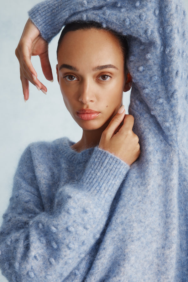 Woman in a denim blue mohair blend bobble jumper with balloon sleeves and crew neck.