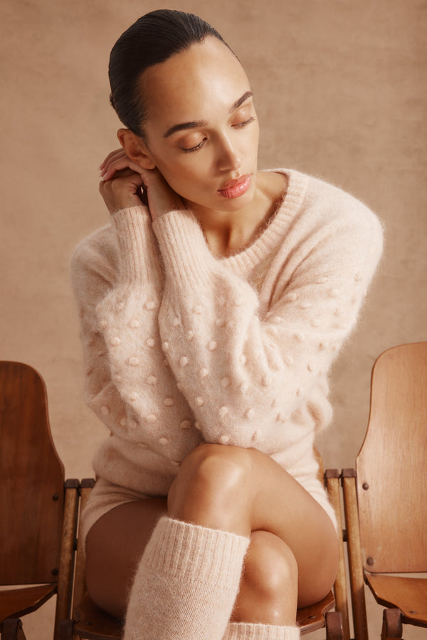 Woman in a nude mohair blend bobble jumper with balloon sleeves, seated.