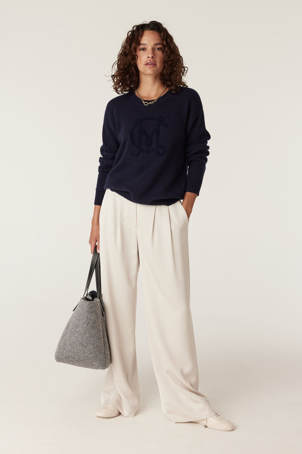 Woman in navy Cashwool logo jumper, cream wide-leg pants, and gray tote bag.