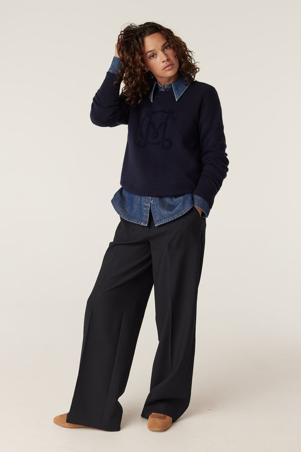 Woman in navy Cashwool logo jumper over a denim shirt and wide-leg trousers.