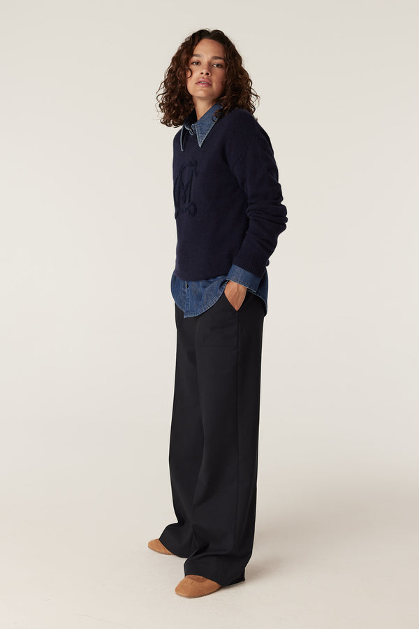 Woman in navy Cashwool logo jumper over denim shirt, black wide-leg pants, and tan shoes.