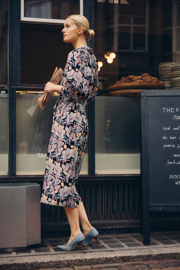 Woman in Leigh Midi Dress, an orchid print silk blend dress with a waist tie and elbow sleeves.