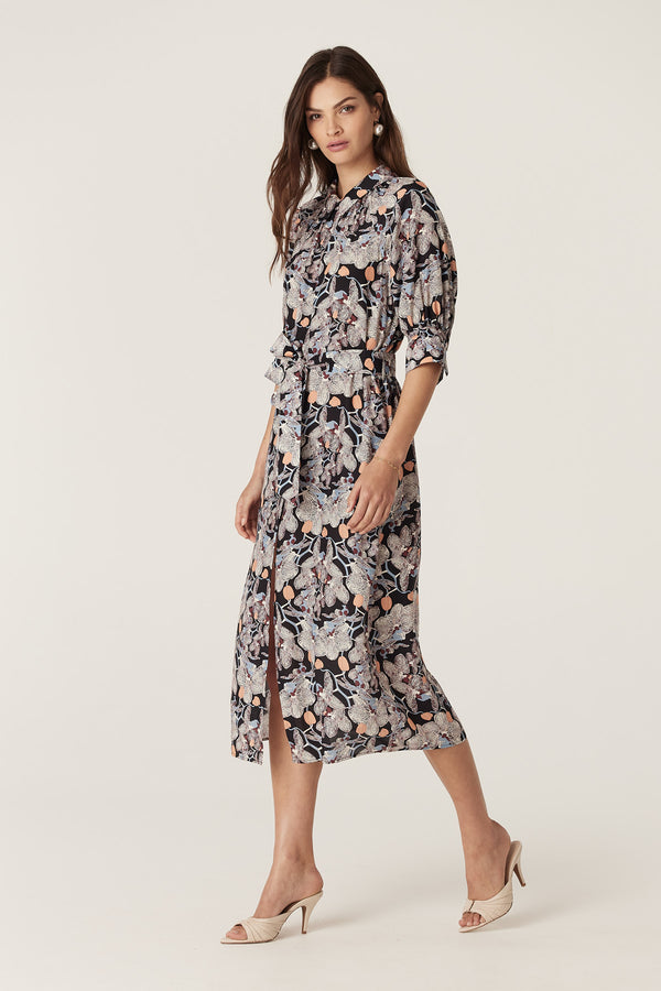 Woman in Leigh Midi Dress, black silk blend with orchid print, shirt collar, button front, and waist tie.