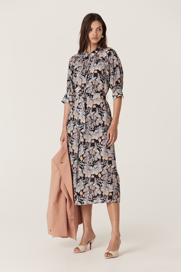 Woman in Leigh Midi Dress, black orchid print silk blend, with shirt collar, button front, and matching waist tie, holding a pink blazer.
