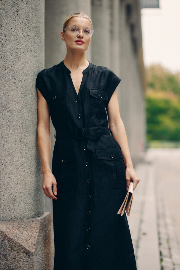 Woman in a black linen blend Osborne dress with utility pockets, D-ring belt, and button-through front.