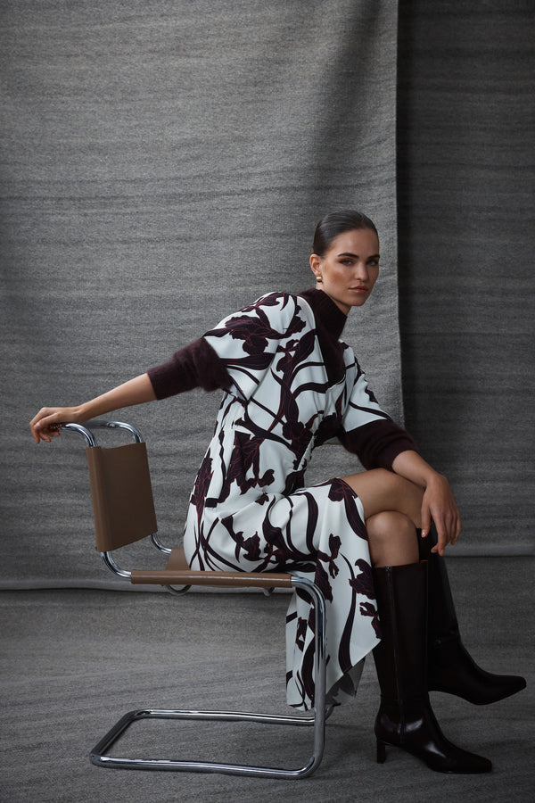 Model in Neve Iris Print dress with V-neck, flared sleeves, and front split, paired with boots.