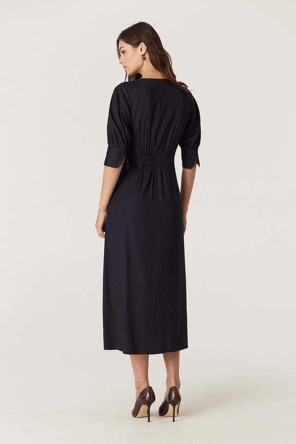 Woman in navy Holly midi dress with elasticated shirring back, elbow sleeves, and wrap waist.