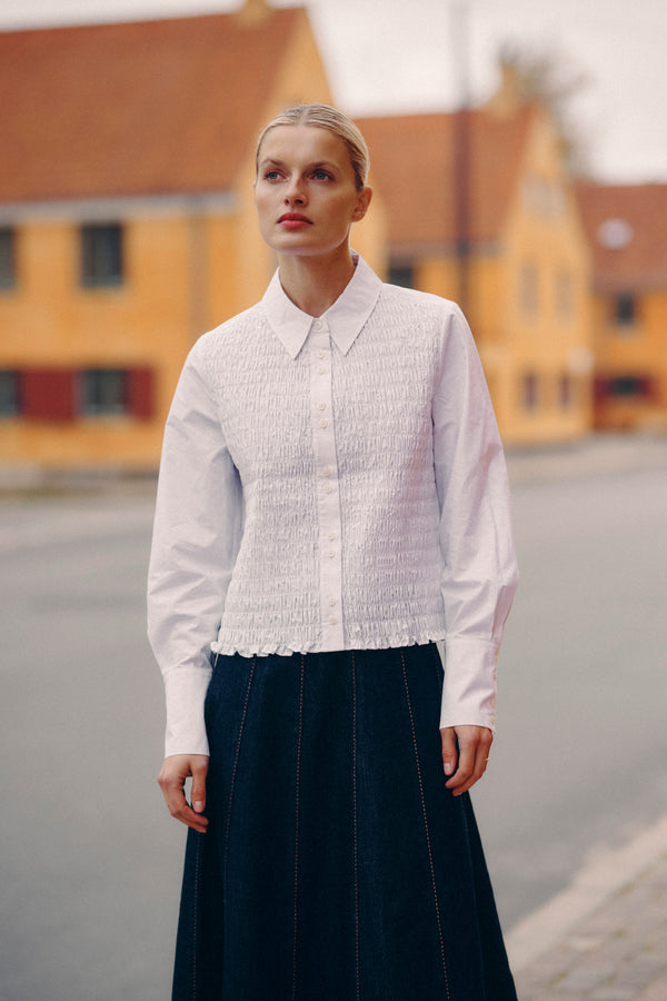 Woman in white crisp cotton May Shirt with shirred front, long sleeves, and structured cuffs.
