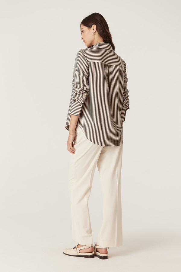 Woman wearing a Jamie Khaki Stripe Shirt with a classic collar, curved hem, and side button detail, paired with cream pants.