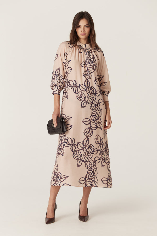 Woman in a relaxed fit Bloom Dress, a light pink silk blend midi dress with dark stencil floral print, stand collar, and raglan sleeves.