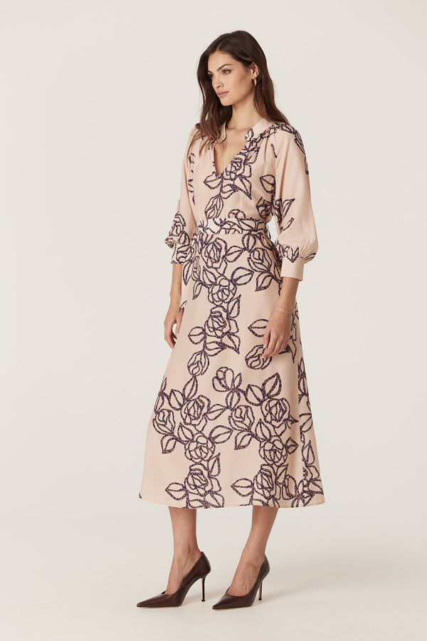 Model wears a relaxed fit Bloom Dress in a light pink silk blend with a dark blue stencil floral print, stand collar, and raglan sleeves.