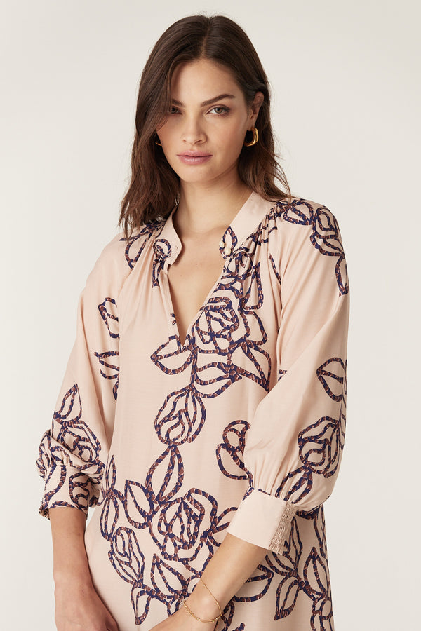 Woman in a relaxed fit Bloom Dress, a light pink silk blend with a dark blue stencil floral print, stand collar, and raglan sleeves.