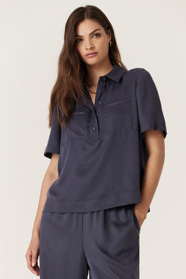 Woman in navy Lyocell Ashton Blouse with half placket, fabric buttons, and front patch pockets.