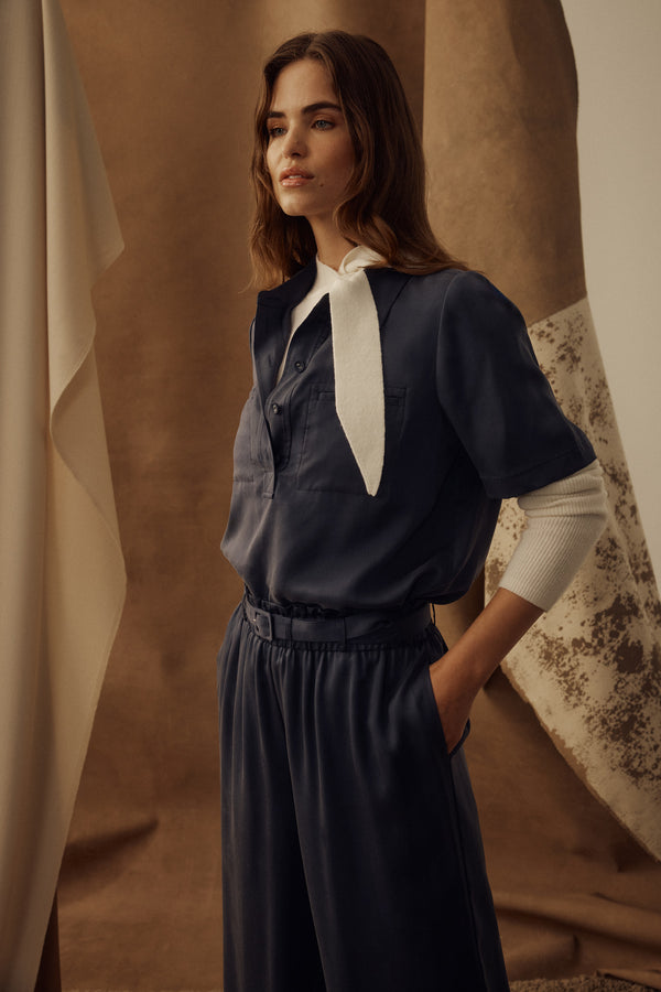 Woman in a navy Lyocell Ashton Blouse with half placket, front pockets, and a white tie detail.