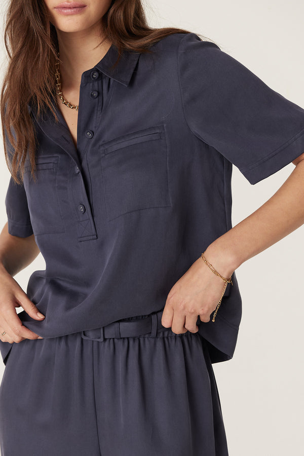 Woman wearing a navy Lyocell Ashton Blouse with half placket, fabric buttons, and front patch pockets.