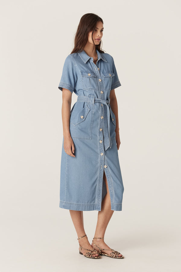 Woman in a blue lyocell cotton Pearce dress with short sleeves, button front, utility pockets, and waist tie.