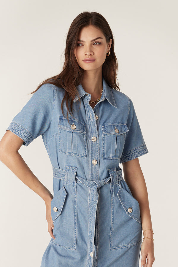 Model wears a blue lyocell cotton blend Pearce Dress with short sleeves, button front, utility pockets, and waist tie.