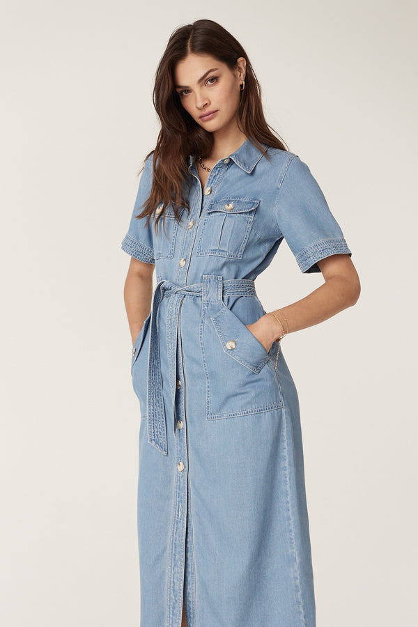Model in a blue lyocell cotton blend Pearce Dress with short sleeves, button front, utility pockets, and waist tie.