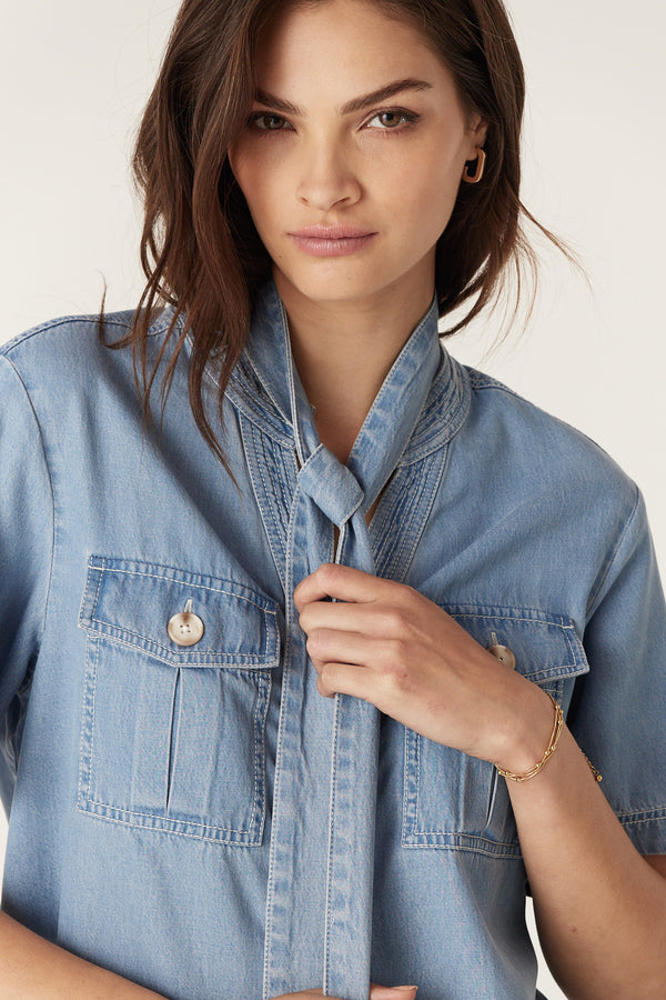 Woman in blue lyocell-cotton Pearce Top with utility pockets, contrast stitching, and a tied front.