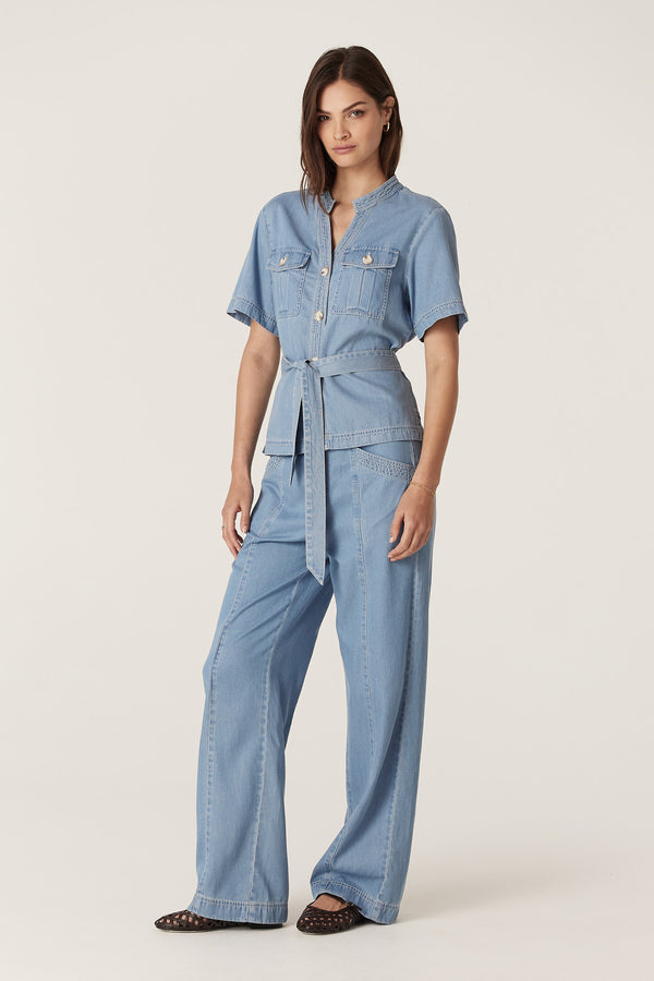 Woman wearing a blue lyocell-cotton Pearce Top and matching pants with utility pockets, contrast stitching, and waist tie.