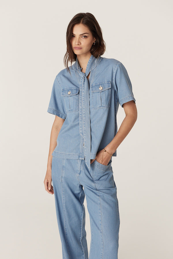 Woman in a blue lyocell-cotton Pearce Top with utility pockets, contrast stitching, and a waist tie.