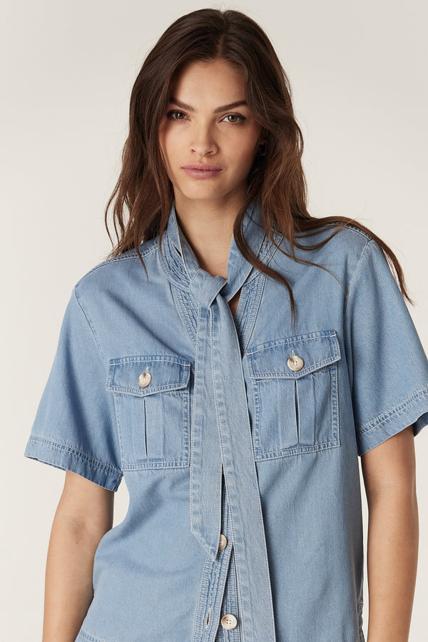 Woman wearing a blue lyocell-cotton Pearce Top with short sleeves, utility pockets, and a tied waist sash.