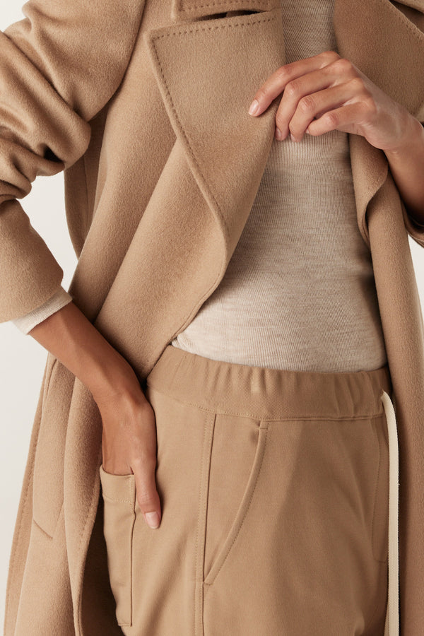 Close-up of a person wearing camel Luca Twill Joggers with an elastic waist, ribbed top, and matching coat.