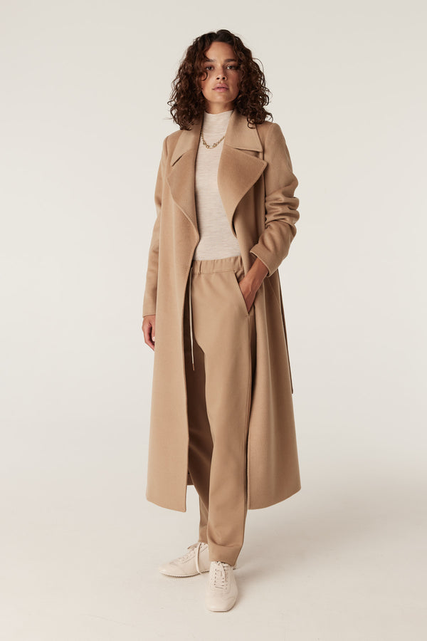 Woman in camel twill joggers, a matching long coat, and a cream turtleneck.