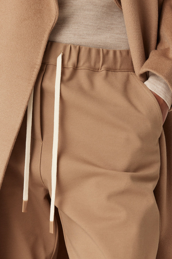 Close-up of camel Luca twill jogger with white drawstring, paired with a ribbed top and wool coat.