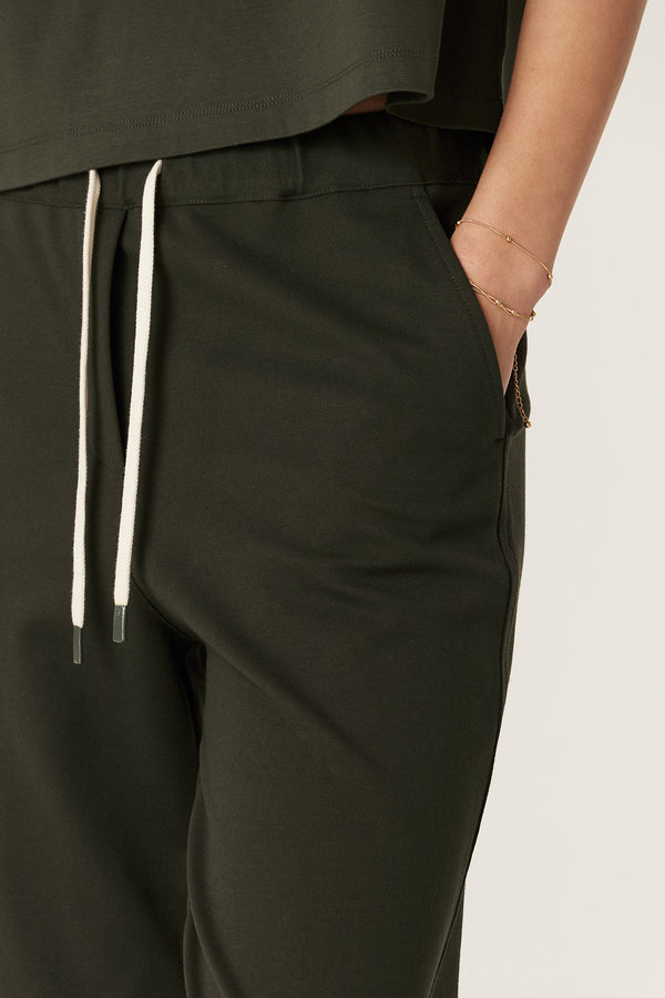 Close-up of forest green Luca Twill Jogger with white drawcord, elastic waist, and hand in pocket.