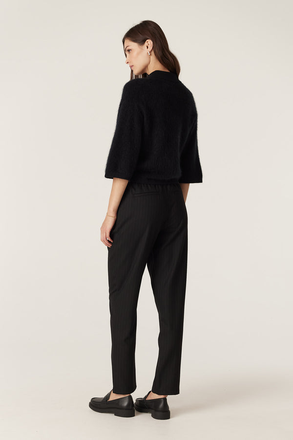 Model wearing black pinstripe Vincent wool pants with elasticated waist and tapered leg.