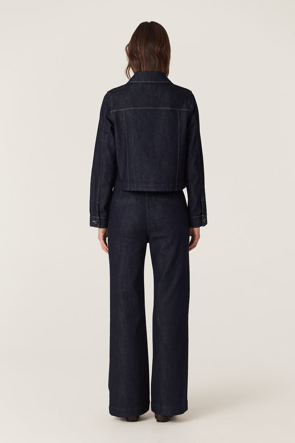 Woman wearing a dark indigo denim jacket with contrast stitching and matching wide-leg jeans.