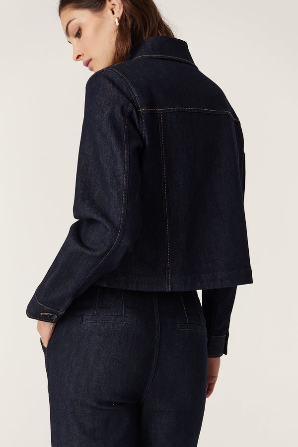 Woman from behind wearing a dark indigo Burke denim jacket with contrast stitching and matching jeans.