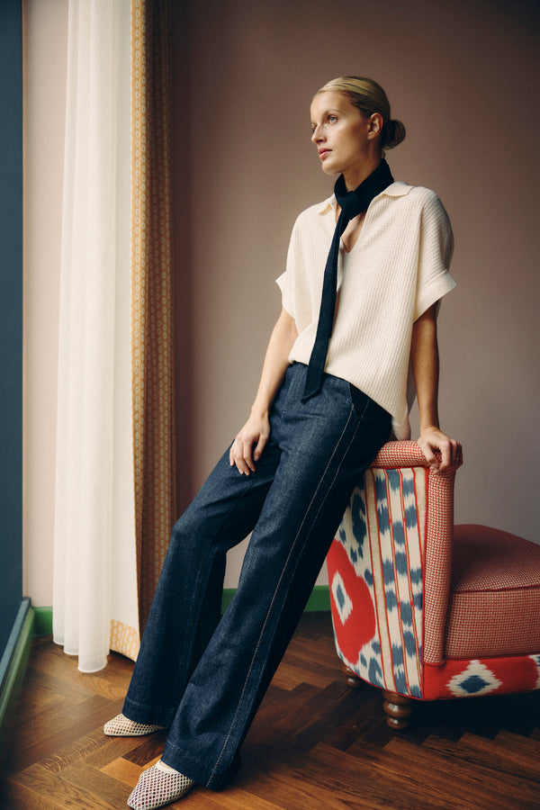 Model in dark indigo Burke jeans with subtle flare and contrast pick stitching, paired with a cream top.