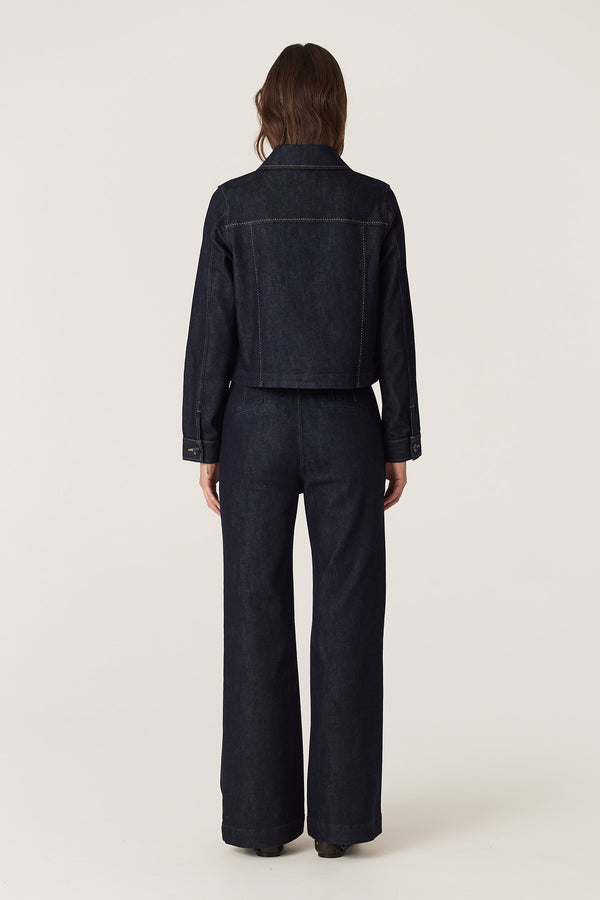 Woman from behind in dark indigo denim jacket and flared Burke jeans with pick stitching.