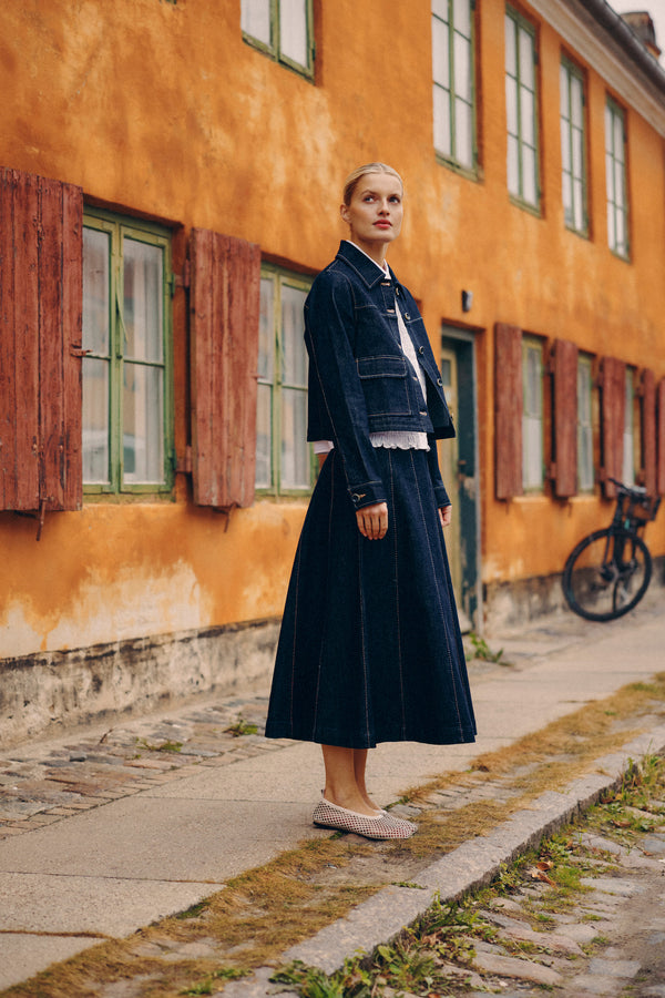 Model in dark indigo Burke denim skirt with gored panels and contrast stitching, paired with a denim jacket.