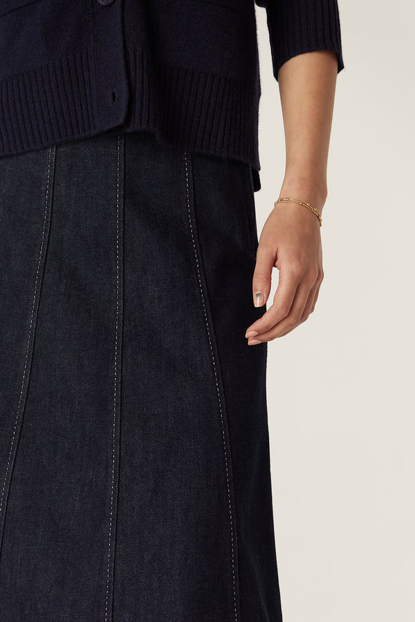 Dark indigo denim skirt with gored panels and contrast white stitching, worn by a model.