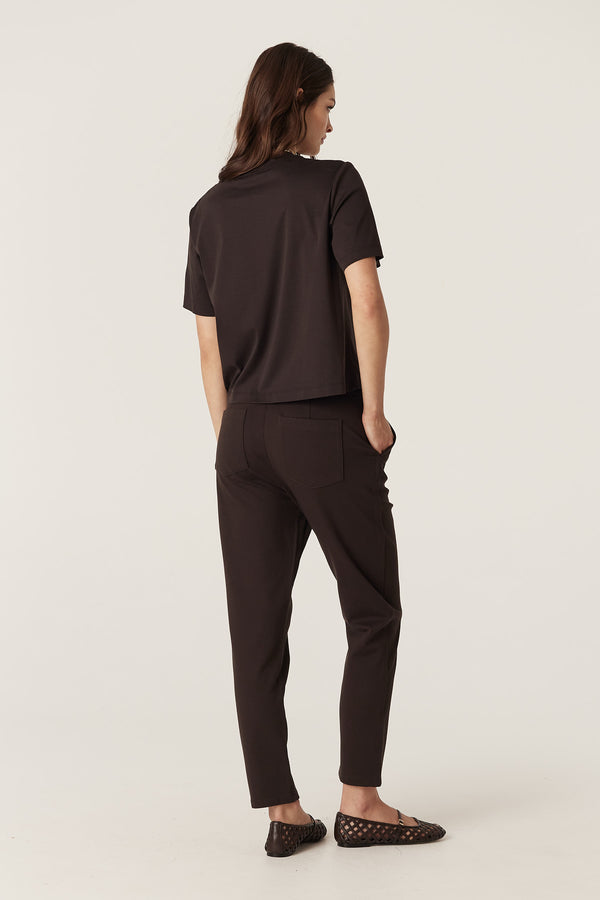 Woman in espresso Pima Boxy Tee and matching pants, viewed from behind, showing relaxed fit and short sleeves.