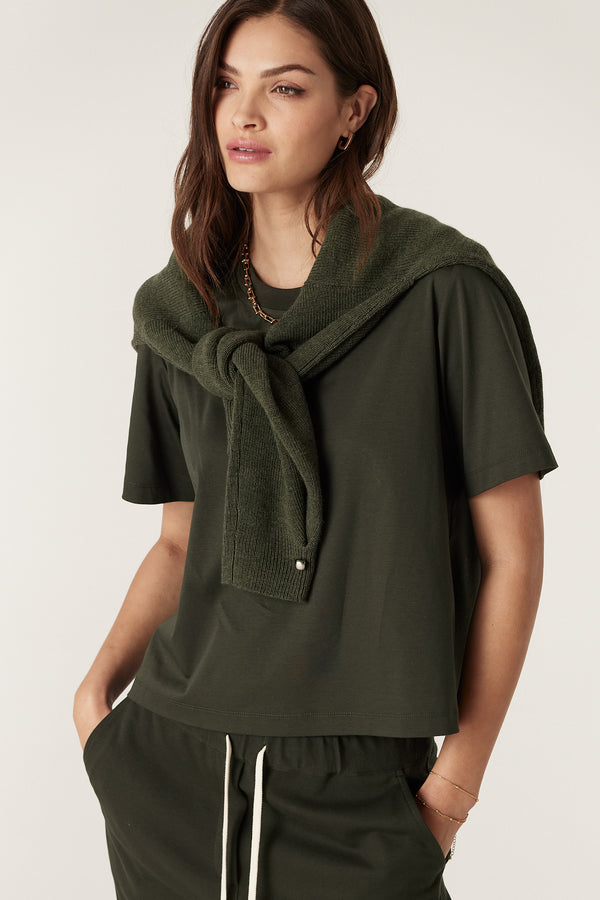 Woman in a relaxed fit forest green Pima Boxy Tee with a matching sweater tied over her shoulders.