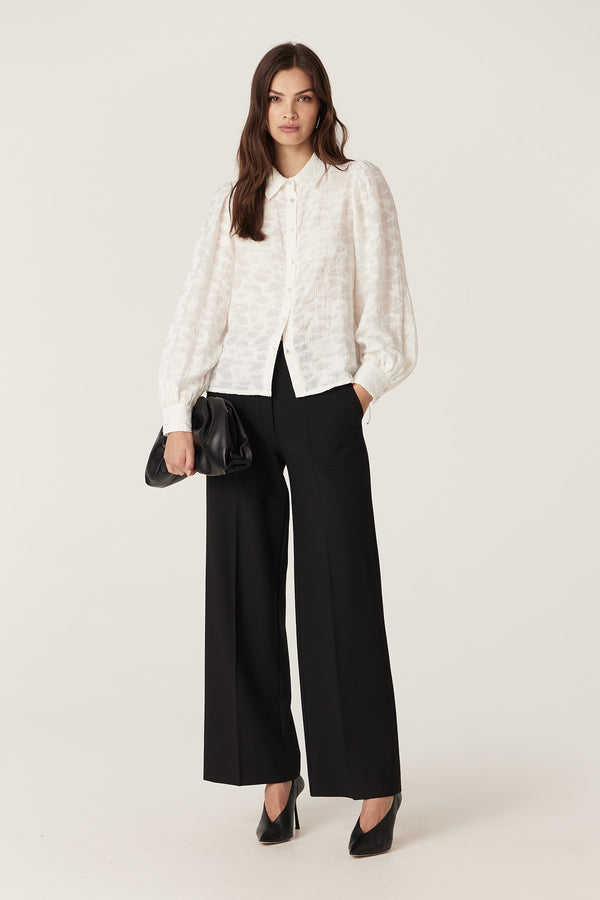 Model wears an ecru Vella Jacquard Blouse with soft sleeve gathers, shell buttons, and black wide-leg pants.