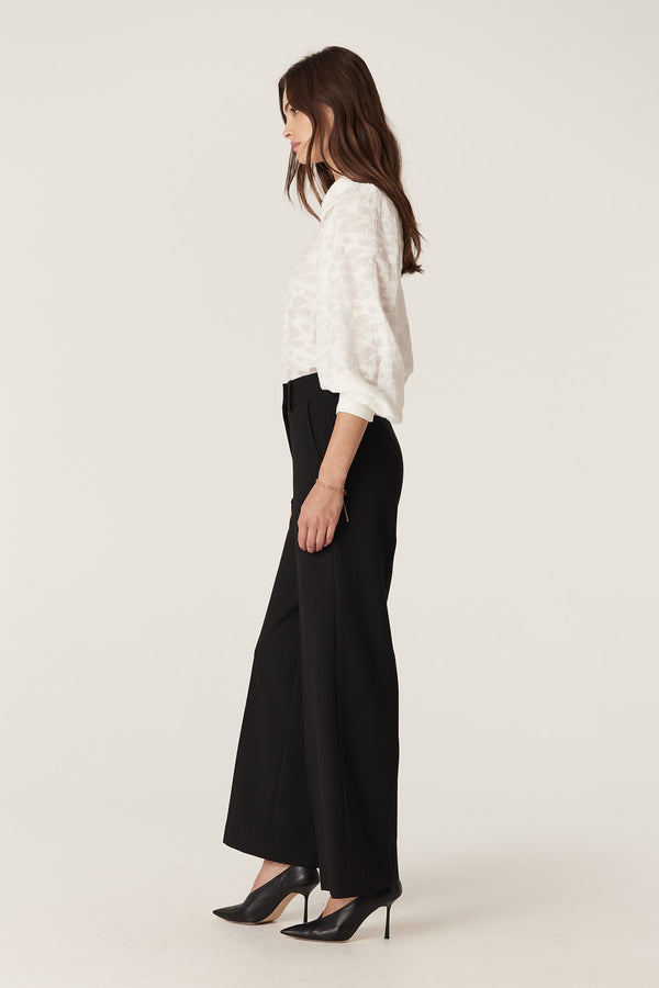 Woman in an ecru Vella Jacquard Blouse with soft sleeve gathers, shell buttons, and black pants.